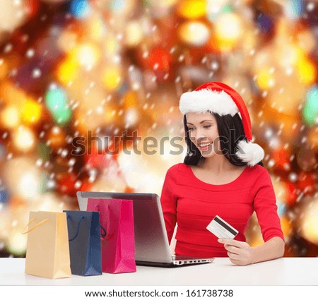 christmas, x-mas, online shopping concept - woman in santa helper hat with shoopping bags, laptop computer and credit card