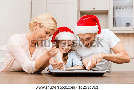 food, family, christmas, hapiness and people concept - smiling family in santa helper hats decorating cookies with glaze