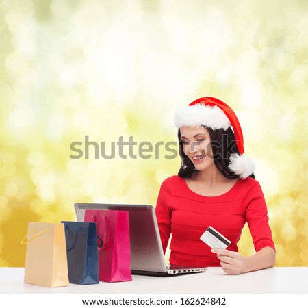 christmas, x-mas, online shopping concept - woman in santa helper hat with shopping bags, laptop computer and credit card