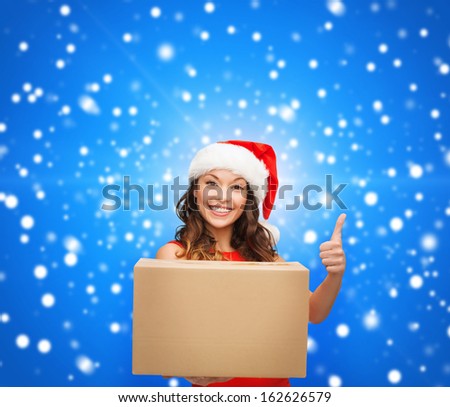 christmas, x-mas, winter, happiness concept - smiling woman in santa helper hat with parcel box showing thumbs up