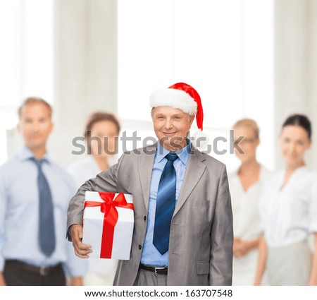 business, christmas, xmas, happiness concept - smiling old man in suit and santa helper hat with gift and team on the back
