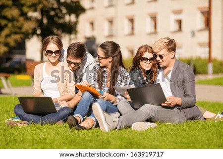 summer, internet, education, campus and teenage concept - group of students or teenagers with laptop, notebooks, files and folders
