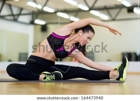 fitness sport training gym and lifestyle concept stretching young woman with earphones in the gym fitness sport training gym and lifestyle concept stretching young woman with earphones in the gym