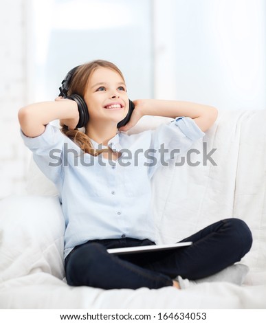 home, leisure, new technology and music concept - smiling little girl with tablet pc computer and headphones at home