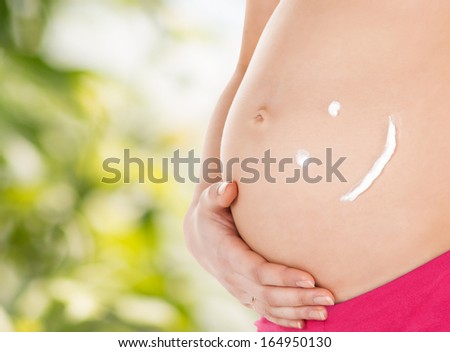 pregnancy, maternity and health concept - belly of a pregnant woman with cream and smile symbol