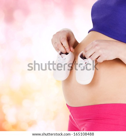 pregnancy, maternity and health concept - belly of a pregnant woman with pink baby booties