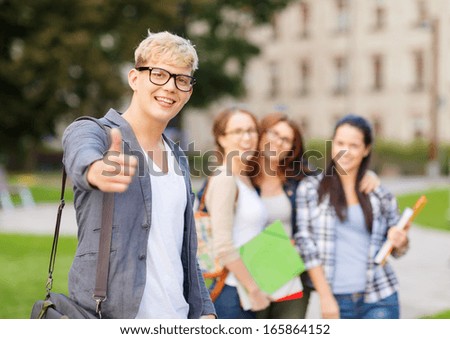 summer holidays, education, campus and teenage concept - smiling male student in black eyeglasses with group in the back showing thumbs up