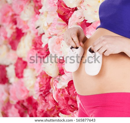 pregnancy, maternity and health concept - belly of a pregnant woman with pink baby booties