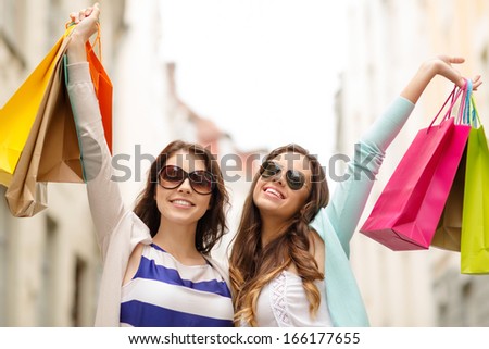 shopping, sale, happy people and tourism concept - smiling girls in sunglasses with shopping bags in ctiy