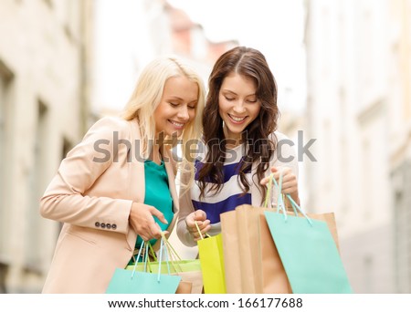 Sale, Shopping, Tourism And Happy People Concept - Two Beautiful Women Looking Inside Shopping Bags In The Ctiy