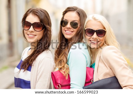 holidays, tourism and happy people concept - three smiling women in sunglasses with bags in the city
