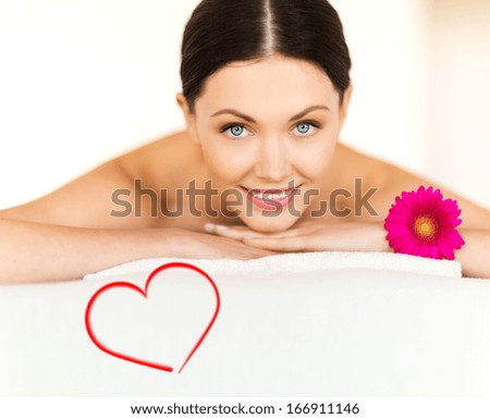 spa, beauty, resort and relaxation concept - smiling woman with flower in spa salon lying on the massage desk