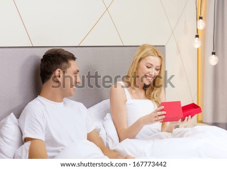 hotel, travel, relationships, holidays and happiness concept - smiling couple in bed with red gift box