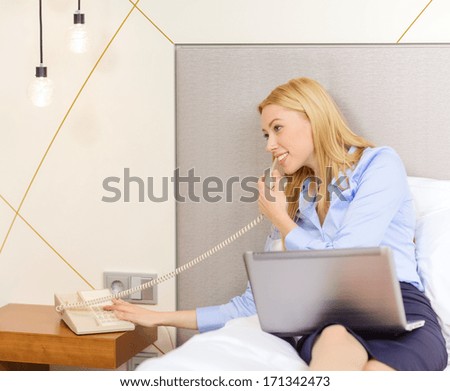 business, technology, internet and hotel concept - happy businesswoman with phone and laptop lying in hotel in bed