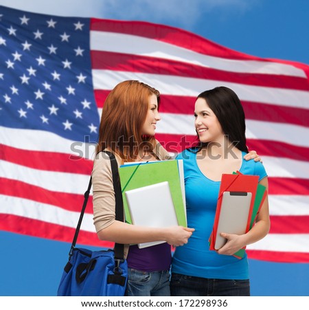 education and people concept - two smiling students with bag and folders looking at each other over american flag background