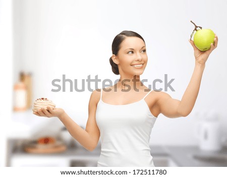 sport and diet concept - sporty woman with apple and cake in kitchen