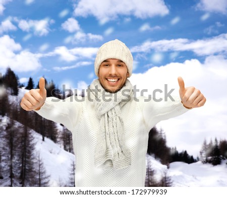 winter holidays, vacation and lifestyle concept - handsome man in warm sweater, hat and scarf showing thumbs up