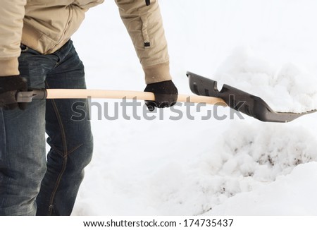 winter and cleaning concept - closeup of man shoveling snow from driveway