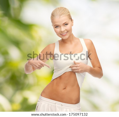 fitness and diet concept - beautiful sporty woman pointing at her abs