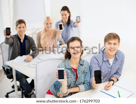 education, school, technology and internet concept - smiling students showing black blank smartphone screens at school