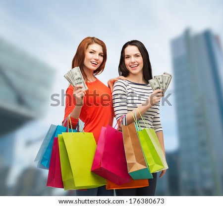 shopping, sale and gifts concept - two smiling teenage girls with shopping bags and cash money