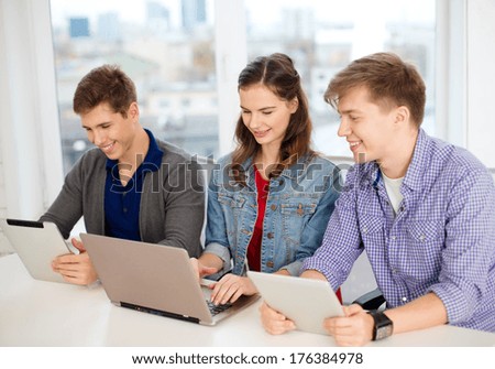 education, technology, school and internet concept - three smiling students with laptop and tablet pc at school