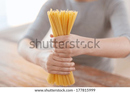 cooking, food and home concept - close up of female hands holding uncooked spaghetti pasta