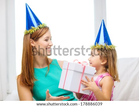 family, children, celebration, holidays, birthday and happy people concept - happy mother and daughter in blue party hats with gift box