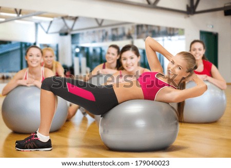 fitness, gym, exercise and health concept - young female instructor doing exercise on fitness ball infront group of people