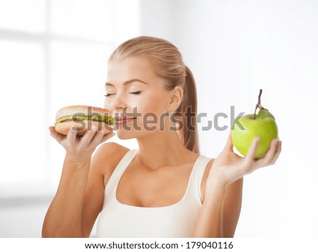 health, diet and food concept - healthy woman smelling hamburger and holding apple