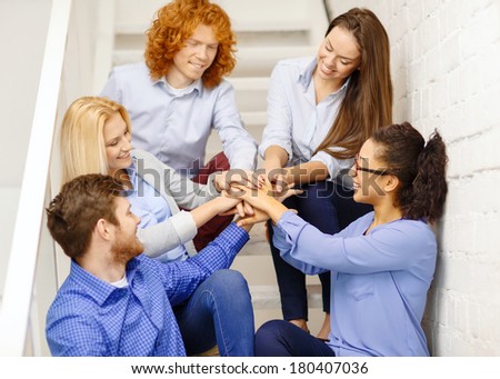 business, office, gesture and startup concept - smiling creative team with hands on top of each other sitting on staircase