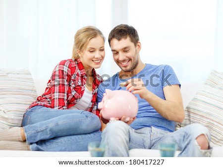 money, home, finance and relationships concept - smiling couple with piggybank sitting on sofa
