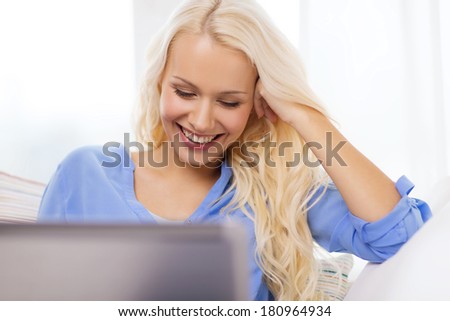 home, technology and internet concept - smiling woman sitting on the couch with laptop computer at home