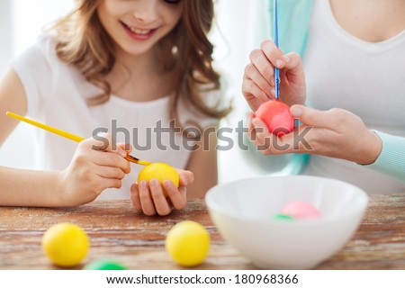 easter, family, holiday and child concept - close up of little girl and mother coloring eggs for easter