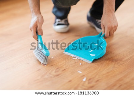 cleaning and home concept - close up of male brooming wooden floor with small whisk broom and dustpan