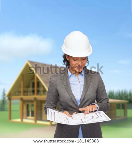 building, developing, consrtuction and architecture concept - smiling businesswoman in white helmet pointing finger to blueprint