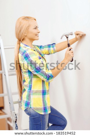 reapir, building and home renovation concept - smiling woman hammering nail in wall