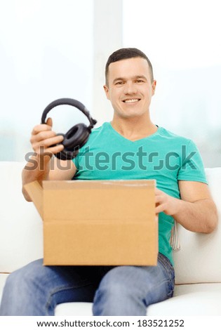 post, home, technology and lifestyle concept - smiling man opening cardboard box with headphones in it