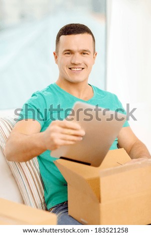 post, home, technology and lifestyle concept - smiling man opening cardboard box with tablet pc computer in it