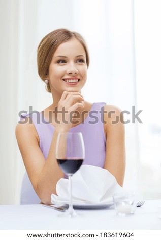 reastaurant and happiness concept - smiling young woman with glass of red whine waiting for date at restaurant