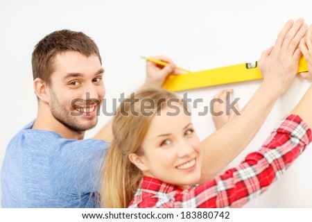 repair, building and home concept - smiling couple building new home using spirit level to measure