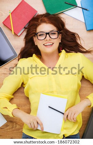 education and home concept - smiling redhead female student in eyeglasses lying on floor with pencil and textbook