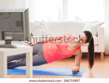 fitness, home and diet concept - smiling teenage girl doing side plank and watching tv at home
