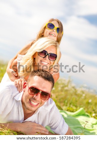 summer holidays, family, child and happy people concept - smiling family in sunglasses lying on blanket outdoors