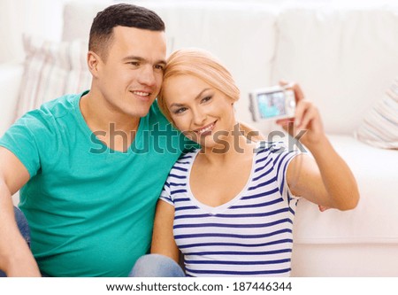 love, family, technology and happiness concept - smiling couple taking self portrait picture with digital camera at home