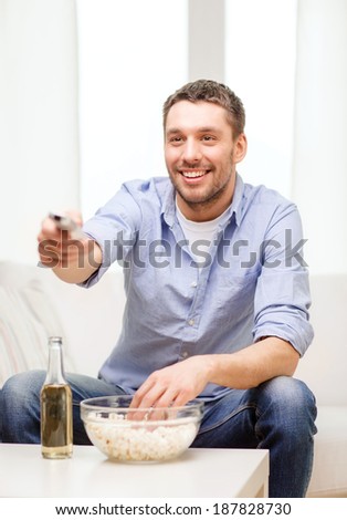home, technology and entretainment concept - smiling man with beer, popcorn and tv remote control at home