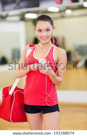 fitness, training, gym, technology and lifestyle concept - smiling woman with sports bag, smartphone and earphones