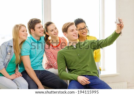 education, leisure and technology concept - five smiling students taking selfie with digital camera at school