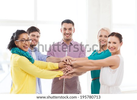 business, office, gesture and startup concept - smiling creative team with hands on top of each other sitting in office