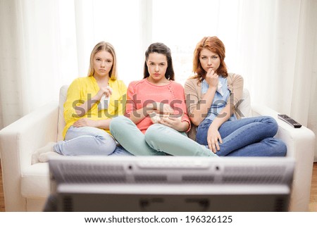 home, technology and friendship concept - three sad teenage girl watching tv at home and eating popcorn
